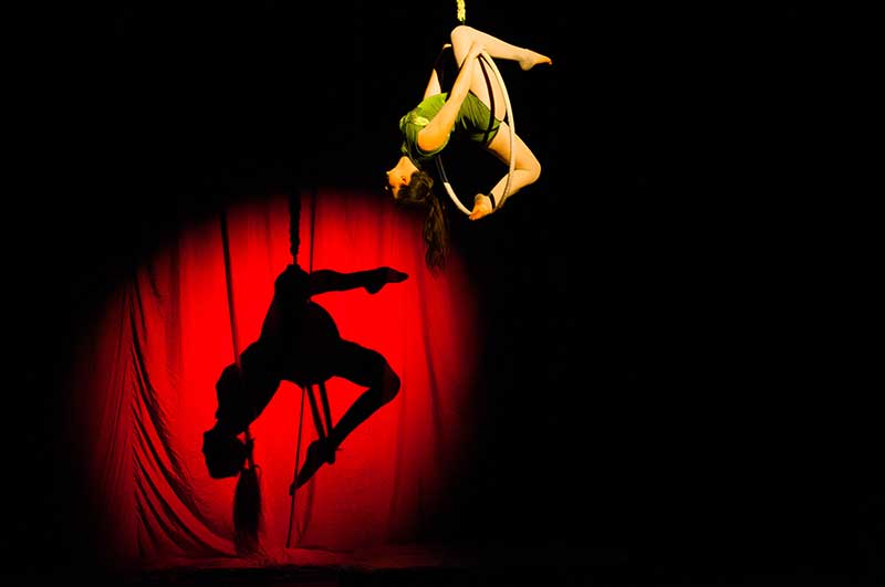 woman upside down hanging with shadow cast onto red show curtains
